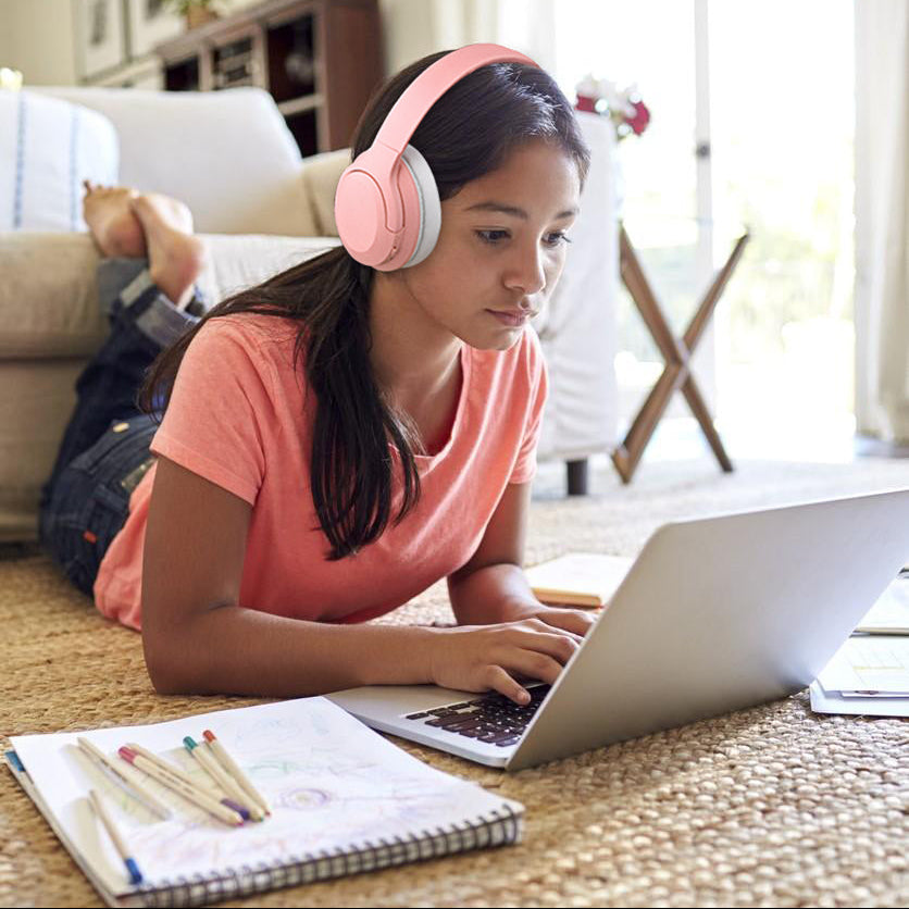 Meisje met roze draadloze kinder koptelefoon met active noise cancelling en bluetooth terwijl ze op een laptop werkt