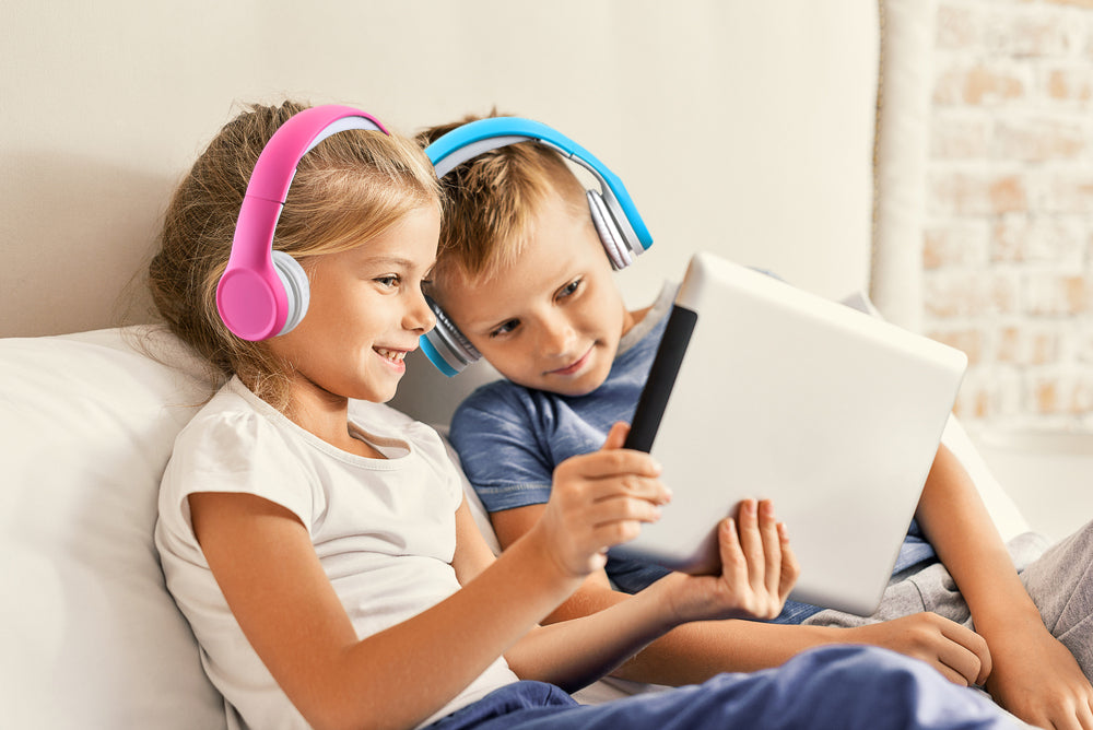 Kinderen met bedrade koptelefoon voor kinderen in roze en blauw terwijl ze samen een tablet gebruiken