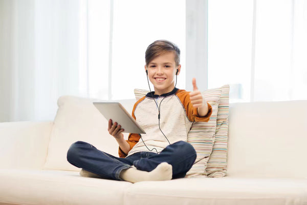 WiseQ bedrade in ear oordopjes koptelefoon voor kinderen in zwart met 3.5mm aansluiting gedragen door jongen met tablet op bank